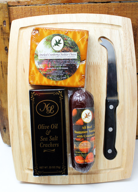 ML7188 Mille Lacs Slice it Up Gift assembled by persons with disabilities on a rectangle cutting board measuring 11x8.5" and containing a stainless cheese knife, and 5oz of Northwoods Cheese All Beef Summer Sausage, 6oz of Northwoods Cheese Smoked Cranberry Cheddar Cheese, and .55oz of Mille Lacs Olive Oil and Sea Salt Crackers.  Shelf Stable and ready to gift