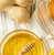 Glass dish with honey and honey dipper next to fresh ginger on a tan striped kitchen towel
