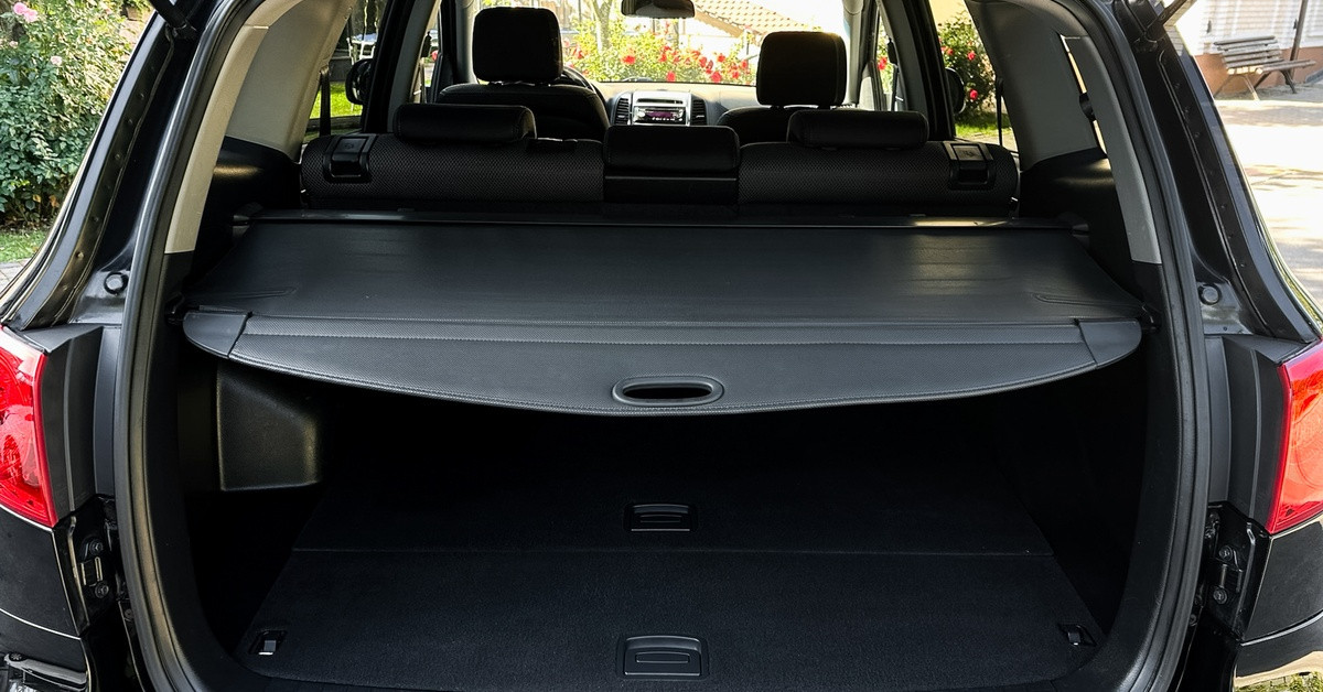 A close-up of a parked black vehicle with the trunk open. The cargo space has a black rear cargo cover.