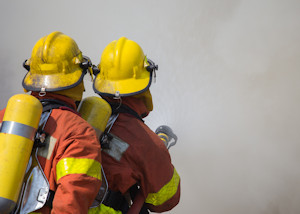 Two firefighters in uniform pointing their hose into smoke.jpg