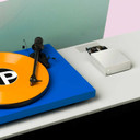 Lifestyle shot of the Pro-Ject Phono Box S2 Phono Preamplifier in silver with a Pro-Ject blue turntable with an orange record