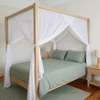 Light timber four poster bed dressed with a cotton mosquito net bed canopy