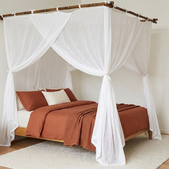 Super king bed with rust-coloured bedding beneath an open cotton box mosquito net
