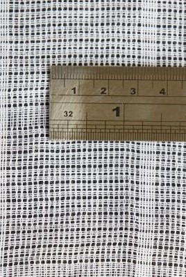 Ruler laid across cotton mosquito netting to show the mesh size up close
