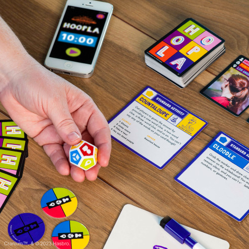 Cranium Hoopla components closeup including a 12-sided category die and an activity card instruction the player how to deliver clues 