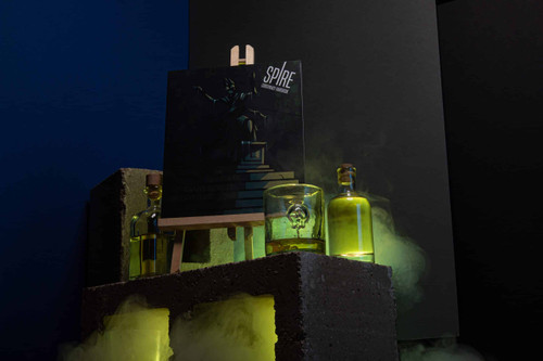 Artistic image of the book on an easel surrounded by glass bottles and mist with a black clothed character on a stone platform