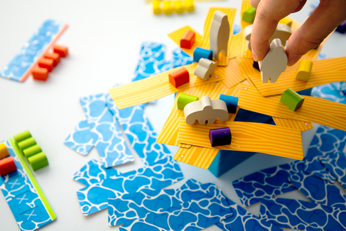 odd shaped meeples on yellow cardboard planks with water appearing under them