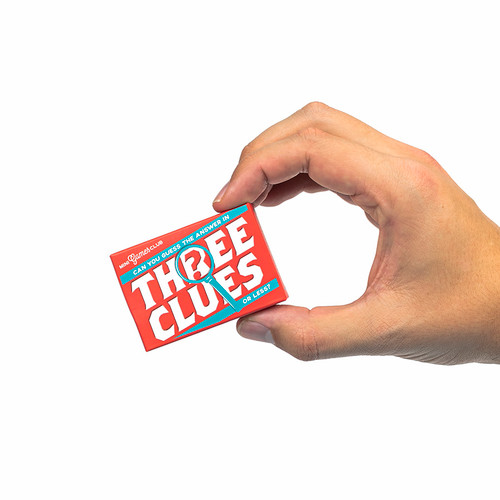 A hand holds one of the games, Three Clues, between two fingers
