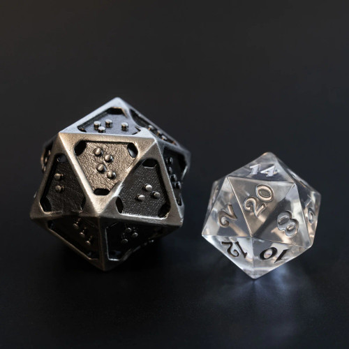A 20-sided die (D20) from the Silver Ingot hollow metal braille dice set is shown alongside a standard clear D20 for size comparison only.  The Silver Ingot hollow metal braille dice are slightly oversized in comparison to a standard die.  (Clear die not included)