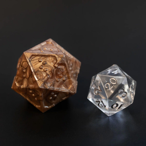 A 20-sided die (D20) from the Acrylic Molten Bronze braille dice set is shown alongside a standard clear D20 for size comparison only.  The Acrylic Molten Bronze braille dice are slightly oversized in comparison to a standard die.  (Clear die not included)