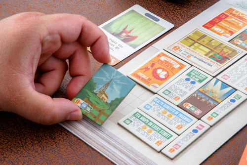 A hand ads a tile to their newspaper page