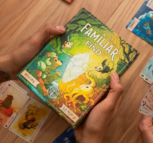 Two hands hold the game box, which depicts cute illustrated animals gathered around a large crystal