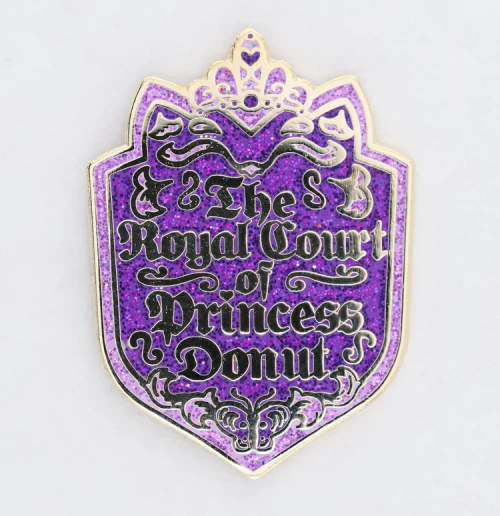 Enamel pin depicting a coat of arms reading "The Royal court of Princess Donut"