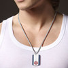 The image shows a close-up of a person wearing a white ribbed tank top and a silver snake chain necklace with a dog tag-style pendant. The pendant features a white center with two vertical dark blue stripes on the sides and a red Star of Life emblem near the bottom, symbolizing medical alert identification. The person’s chest and lower face, including light stubble, are visible, while the background is dark and out of focus, emphasizing the necklace and pendant. The image shows a close-up of a person wearing a white ribbed tank top and a silver snake chain necklace with a dog tag-style pendant. The pendant features a white center with two vertical dark blue stripes on the sides and a red Star of Life emblem near the bottom, symbolizing medical alert identification. The person’s chest and lower face, including light stubble, are visible, while the background is dark and out of focus, emphasizing the necklace and pendant.