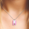 The image shows a close-up of a person’s upper chest and neck wearing a silver medical alert necklace. The necklace features a smooth silver chain and a rectangular dog tag-style pendant with a white center and two vertical pink stripes on the sides. Centered on the white area is a red Star of Life symbol, indicating its medical alert purpose. The person has light-colored hair visible near the neck and shoulder, and the background is softly lit, emphasizing the necklace and pendant. The image shows a close-up of a person’s upper chest and neck wearing a silver medical alert necklace. The necklace features a smooth silver chain and a rectangular dog tag-style pendant with a white center and two vertical pink stripes on the sides. Centered on the white area is a red Star of Life symbol, indicating its medical alert purpose. The person has light-colored hair visible near the neck and shoulder, and the background is softly lit, emphasizing the necklace and pendant.