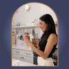 A smiling woman with dark hair is using a white smartphone in a modern kitchen. She wears a black sleeveless top, light-colored pants, and a silver bracelet with a heart-shaped charm on her left wrist. The kitchen features white cabinets, a countertop with a ceramic mug, hanging utensils, a wooden cutting board, and a shelf with glasses and bottles. A round light fixture is visible above the shelf. The scene is framed by a glossy, metallic gold arched border set against a dark blue background, creating an elegant and polished look. A smiling woman with dark hair is using a white smartphone in a modern kitchen. She wears a black sleeveless top, light-colored pants, and a silver bracelet with a heart-shaped charm on her left wrist. The kitchen features white cabinets, a countertop with a ceramic mug, hanging utensils, a wooden cutting board, and a shelf with glasses and bottles. A round light fixture is visible above the shelf. The scene is framed by a glossy, metallic gold arched border set against a dark blue background, creating an elegant and polished look.