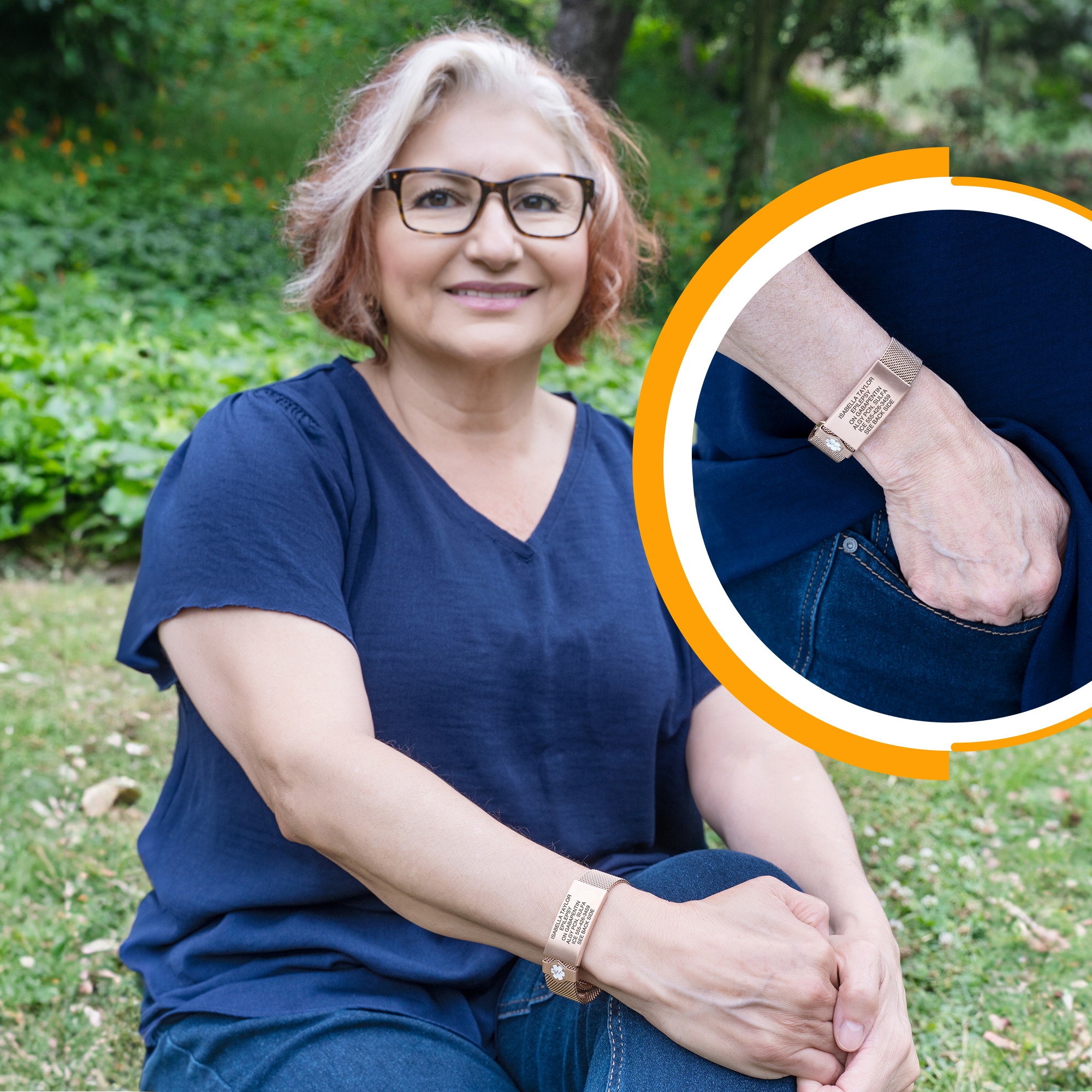 A smiling woman with shoulder-length red and white-blonde hair sits cross-legged on green grass in an outdoor setting, wearing a navy blue V-neck top and jeans. On her left wrist, she wears a rose-gold mesh medical alert bracelet with a rectangular ID plate engraved with her name, "Isabella Taylor," medical details like "Epilepsy," medication, allergies, and an emergency contact number. A circular inset in the upper right corner shows a close-up of the same bracelet on a right arm, highlighting its elegant design and clear engraving. The inset is framed with an orange and white border, drawing attention to the bracelet's details.
