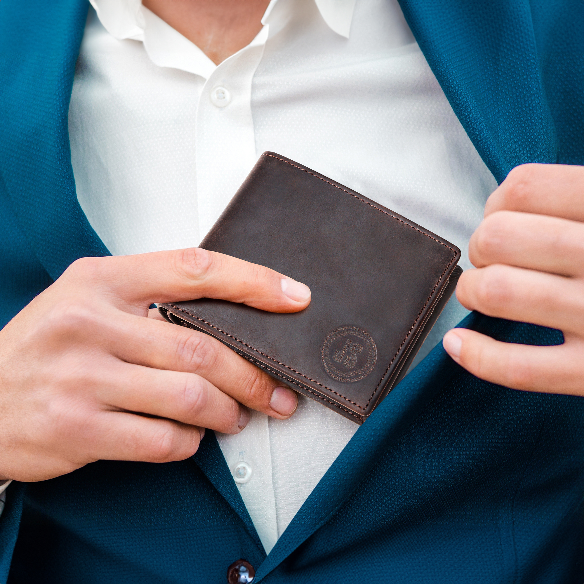 Dark brown leather wallet with visible stitching and a circular monogram logo, being handled by a person in a teal suit and white shirt, emphasizing sophistication and quality.