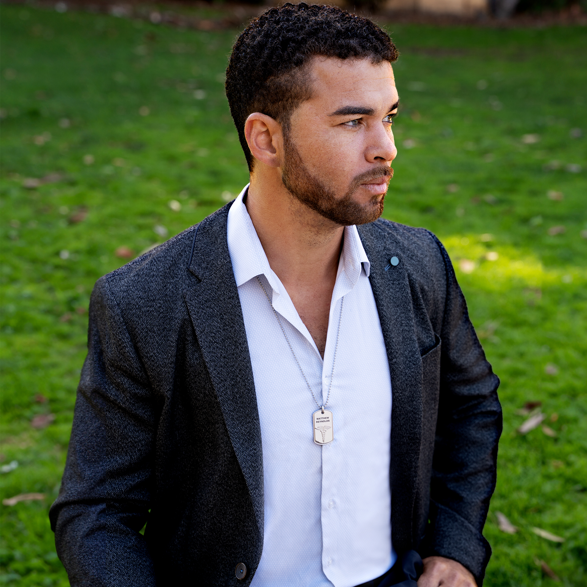 Man wearing a silver dog tag necklace engraved with the name 'Matthew Reynolds' and a medical symbol, paired with a sleek ball chain for a professional and stylish look.