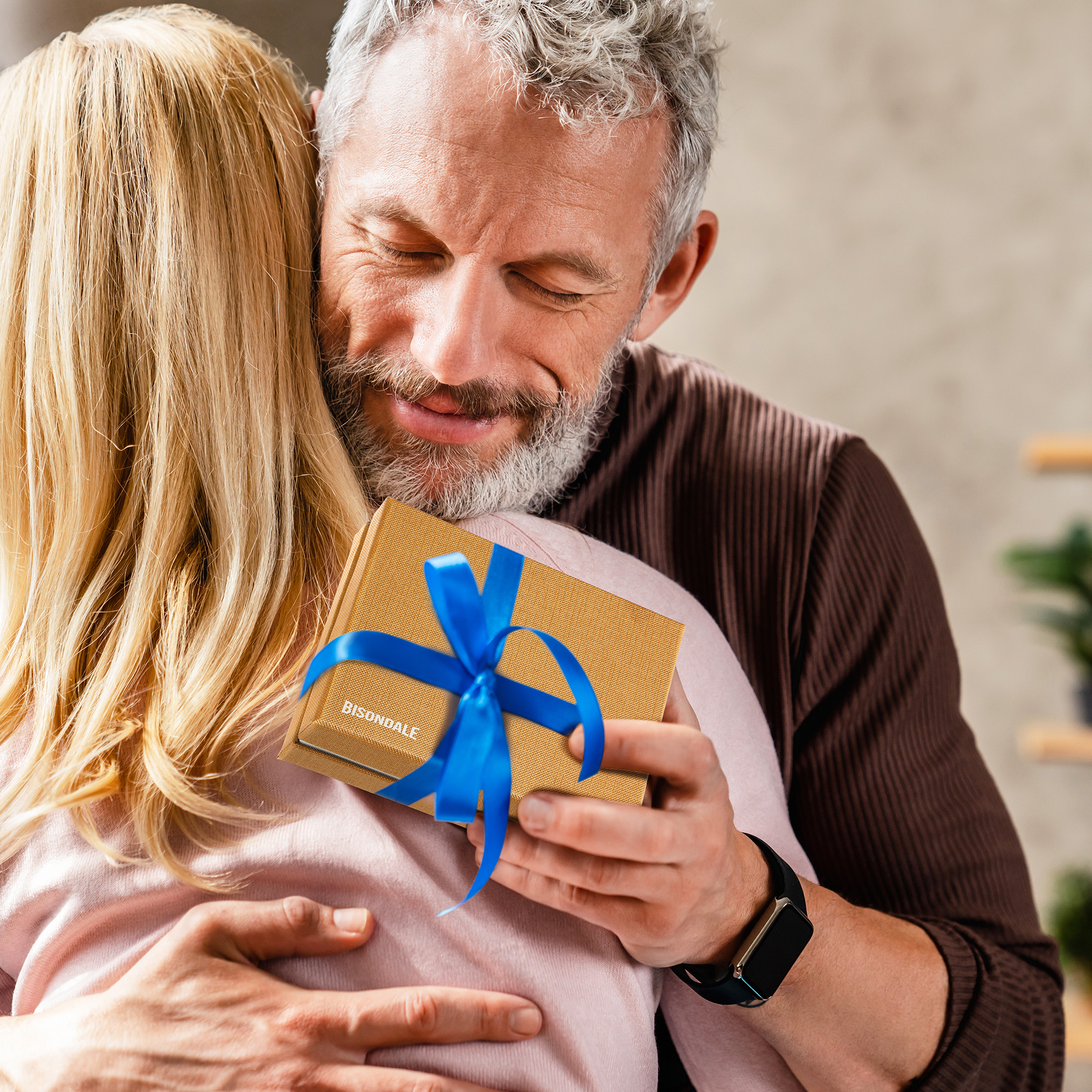 Golden-brown gift box with a textured surface and a vibrant blue ribbon, held by a man embracing a woman, creating a warm and emotional moment.