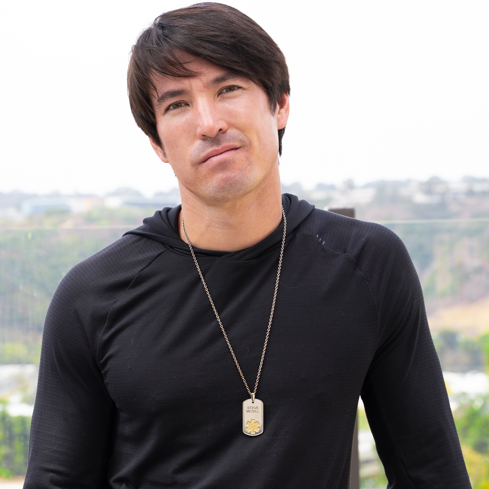 Portrait of a man wearing a silver dog tag necklace with a gold medical symbol, designed for emergency identification and personalized engraving.