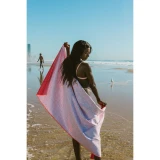 Beach lifestyle image showing a person holding a white and red patterned rPET sand-free beach towel while standing at the shoreline.