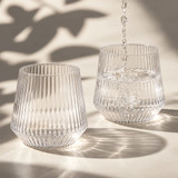 A drink bottle featuring a ribbed design, made of clear glass, with water being poured into two glasses.
