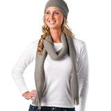 A woman wearing a grey knitted scarf and beanie, with her hair cascading down and a white long-sleeve top.