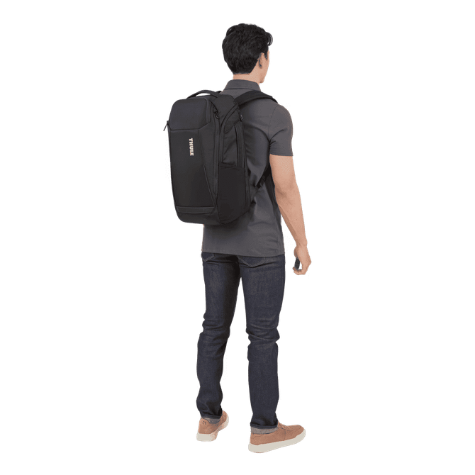 A black backpack worn on the back of a person dressed in a grey shirt and jeans. The backpack features a logo.