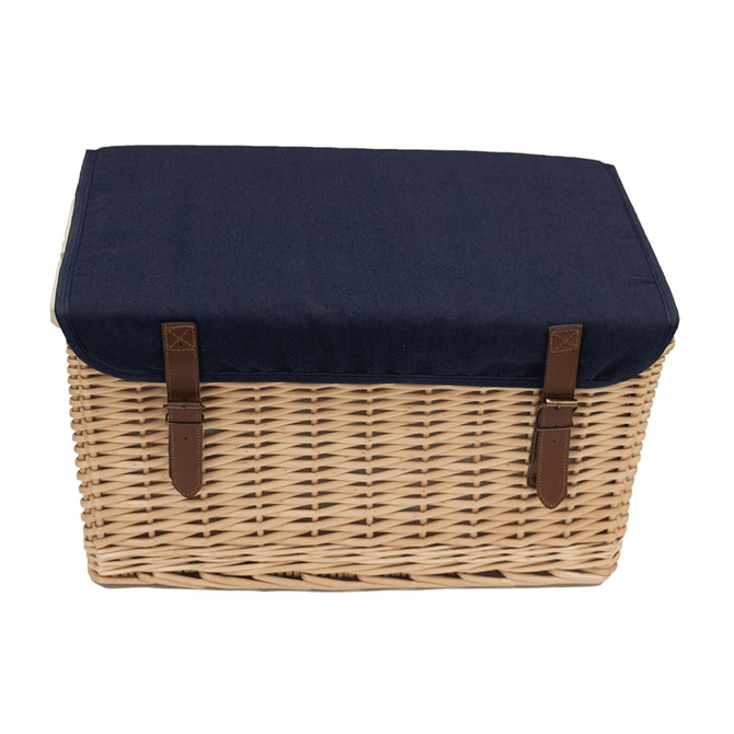 A wicker picnic basket with a navy blue fabric lid and brown leather straps, featuring a logo on the front.