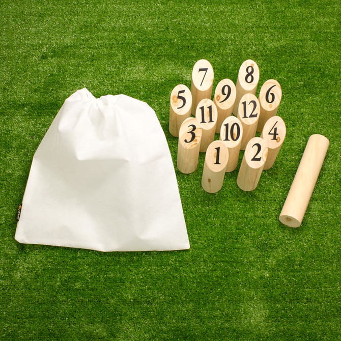 A set of wooden skittles with numbers, a throwing stick, and a white drawstring bag, arranged on grass.