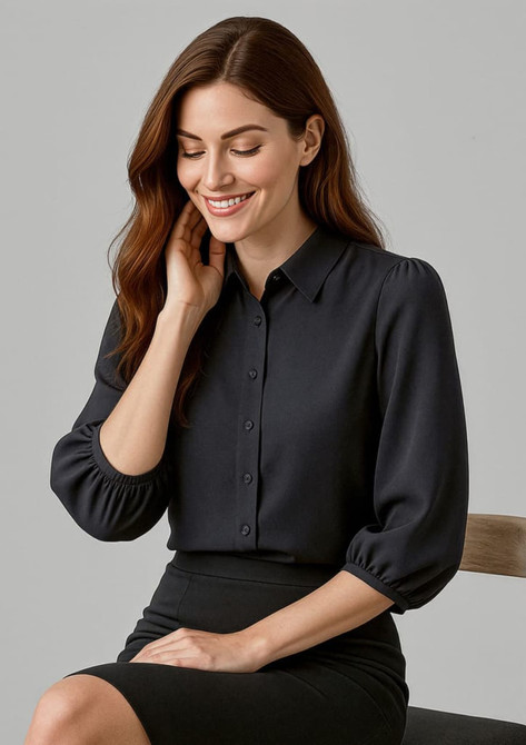 A woman in a black 3/4 sleeve blouse with a button front, sitting on a chair, smiling.