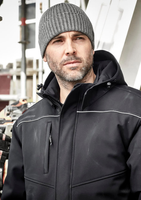 A grey beanie worn by a man in a black jacket, with an industrial background. The beanie features a logo.