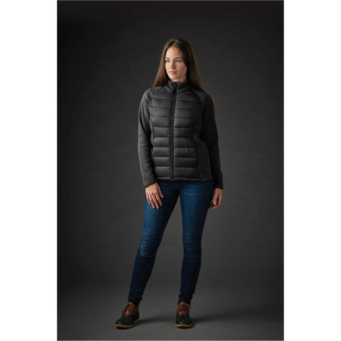 A woman wearing a black hybrid jacket with a padded front and textured sleeves, paired with denim jeans.