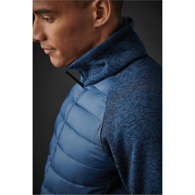 A close-up of a man's blue hybrid jacket featuring a puffy section and textured sleeves. It includes a logo.