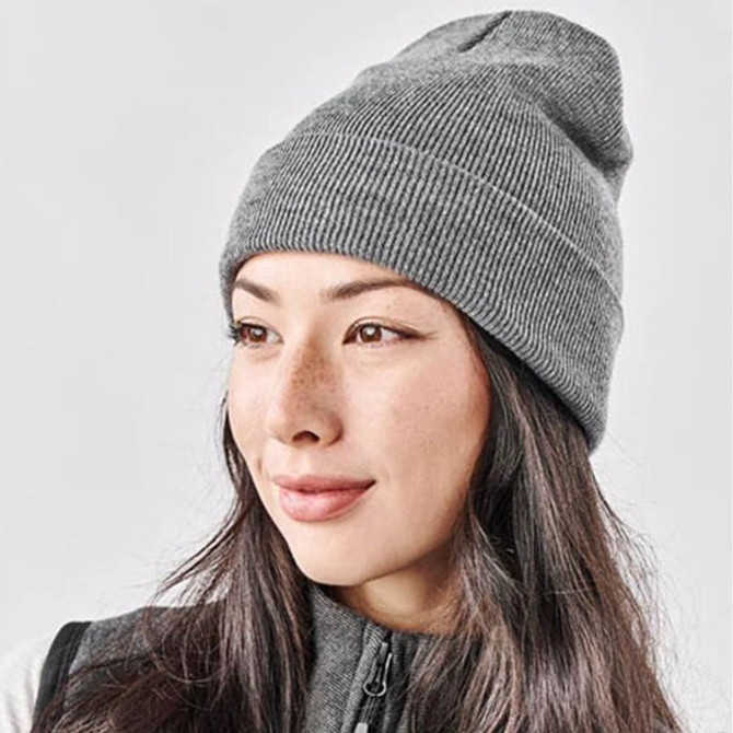 A grey knit beanie worn by a woman with long hair, featuring a subtle logo on the side.