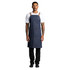 A denim apron featuring tan straps, worn by a person standing upright against a white background.