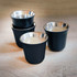 A set of four black espresso cups with metallic silver interiors, featuring a simple design and a logo.