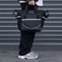 A cooler bag in black with strap and handles, featuring a logo, held by a person near a grey backdrop.