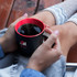 A two-tone mocha coffee mug with a black exterior and red interior, held by a person with grey socks.
