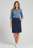 A woman in a blue shirt and navy Lawson skirt, standing confidently with one hand on her hip.