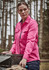 A women's long sleeve button-up shirt in vibrant pink, featuring a logo, set against a forest backdrop.