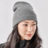 A grey knit beanie worn by a woman with long, dark hair, featuring a simple design and a logo.