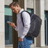 A man wearing a grey Swissdigital Cosmo 3.0 backpack checks his phone outdoors. The backpack features a logo.