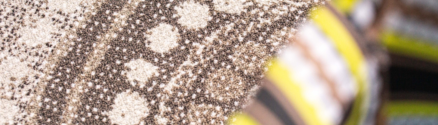 Close-up of a textured carpet with a circular pattern of white and brown dots. A colorful, striped fabric partially covers the right side.
