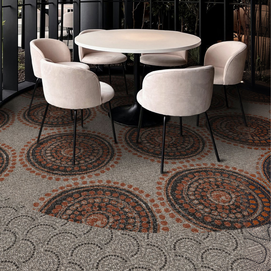 A chic cafe setting with soft beige chairs encircling a round white table. The textured carpet features intricate patterns in orange and black, adding elegance.