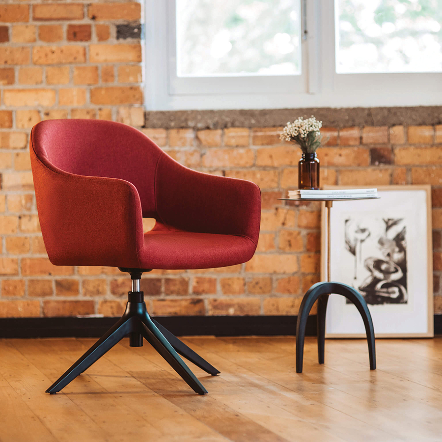 A modern soft red chair with black legs sits on a wooden floor.