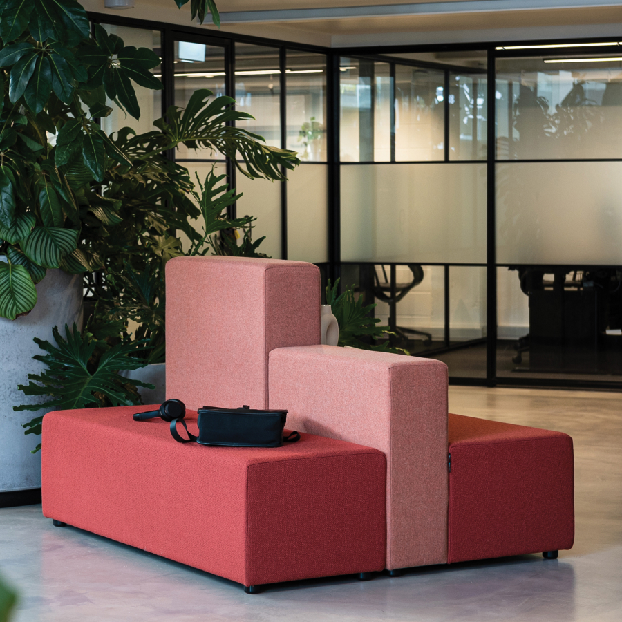 Red and pink modular soft seating in a modern office, surrounded by lush green plants.
