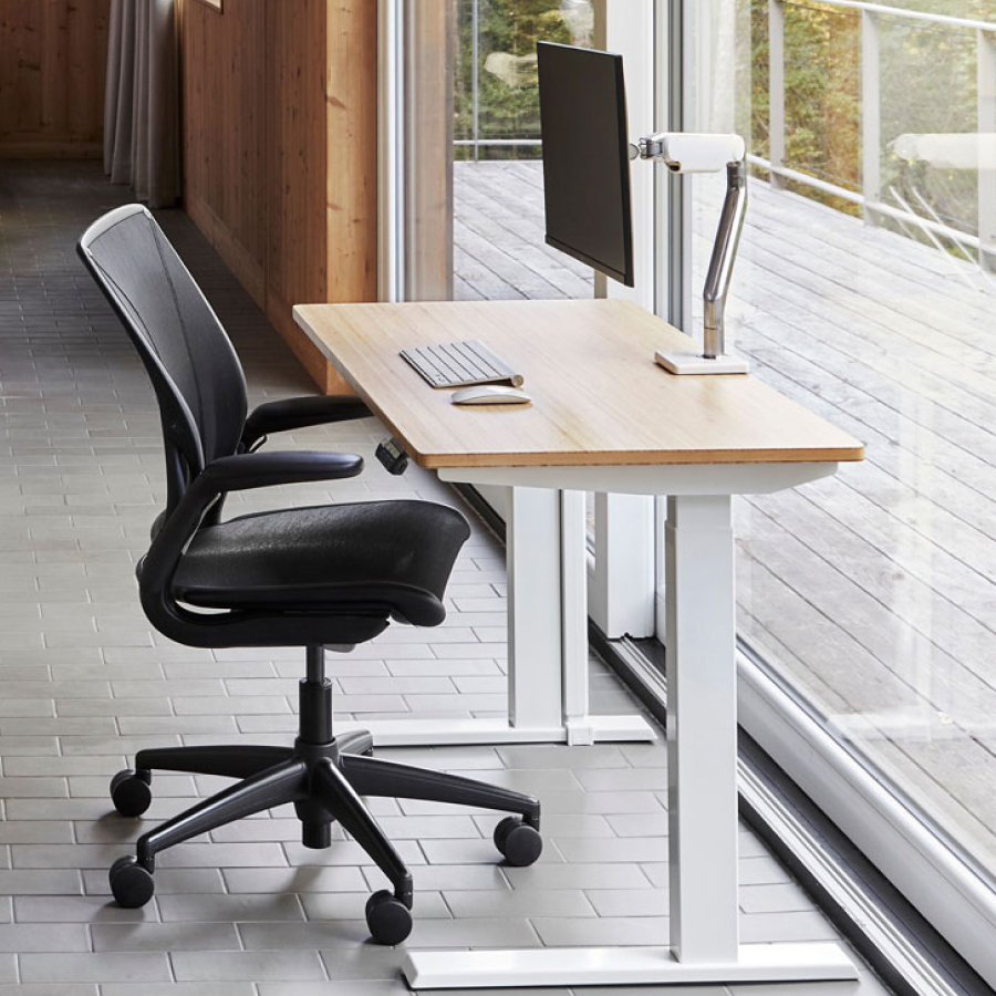 A modern workspace featuring a wooden desk with a computer monitor on an adjustable arm, a keyboard, and a mouse.