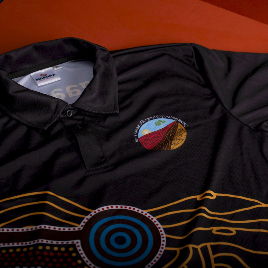Black polo shirt with colorful Aboriginal design and logo on the chest.